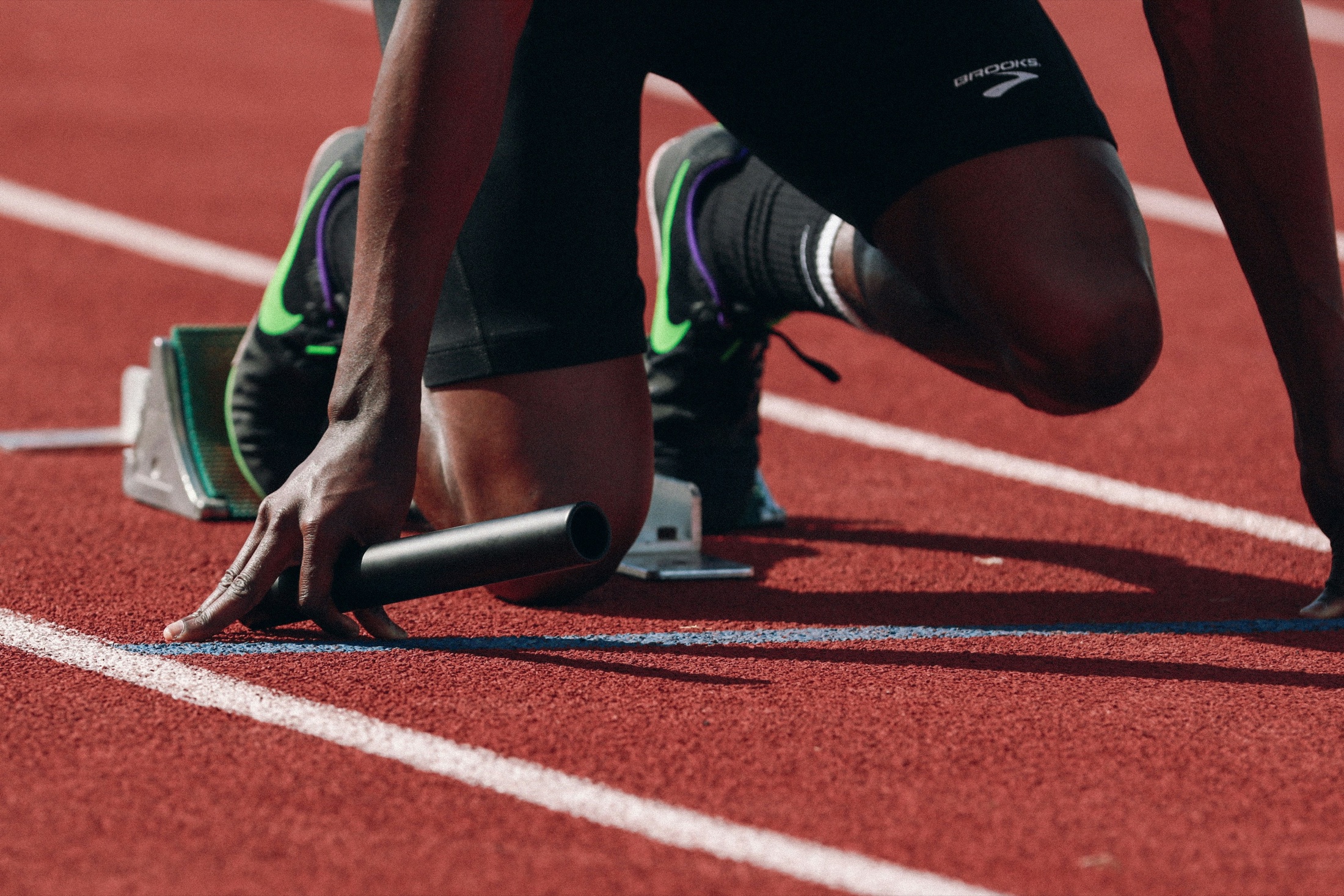 A relay runner holding a baton at the starting blocks on a running track.